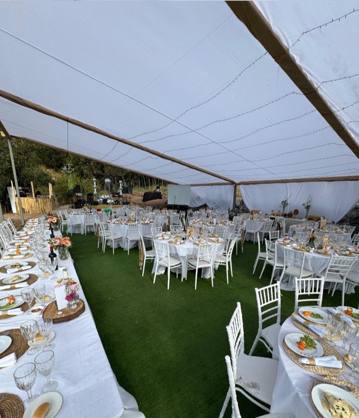 Mesas montadas bajo la carpa, con mantelería y cristalería