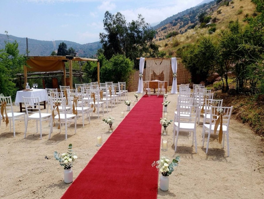 Sillas blancas a ambos lados de una alfombra roja, montadas para una ceremonia frente al cerro