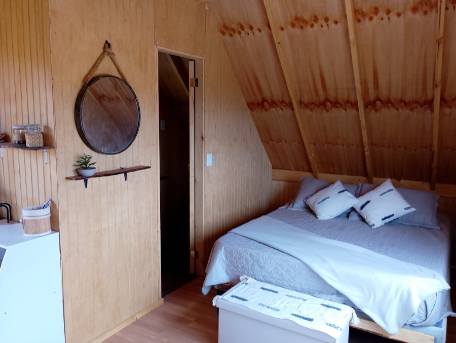 Dormitorio revestido en madera clara con cama de dos plazas y ropa de cama blanca