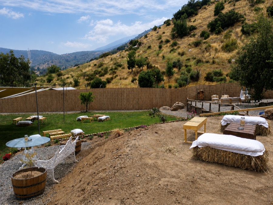El pasto con sillones de fardo, mesas bajas y muebles de fierro blanco, con el cerro detrás