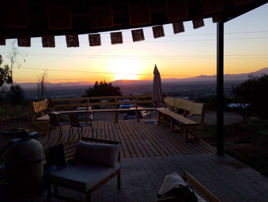 Terraza techada del quincho al atardecer, con parrilla y bancas de madera mirando al valle